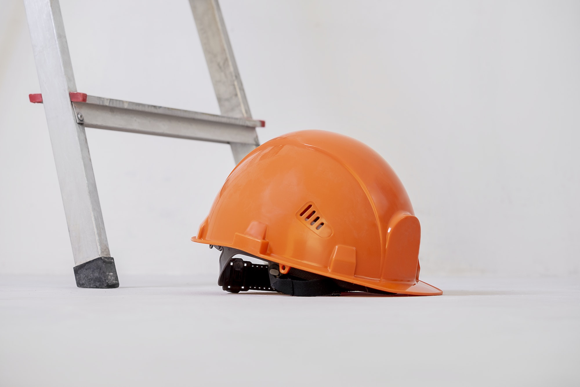 Construction helmet is lying next to stepladder against plaster wall.