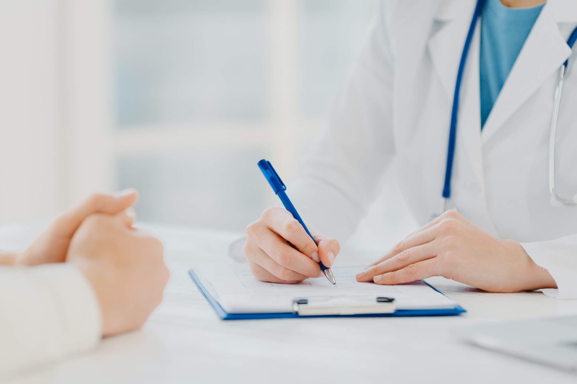 Unknown female doctor writes down prescription on papers in clipboard, consults patient about curing