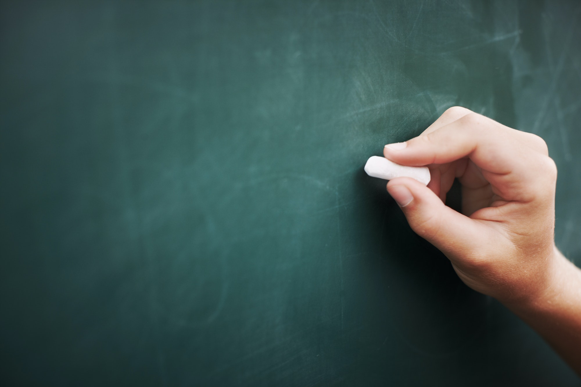 Cropped image of a young boys hand writing on a blackboard with a piece of chalk
