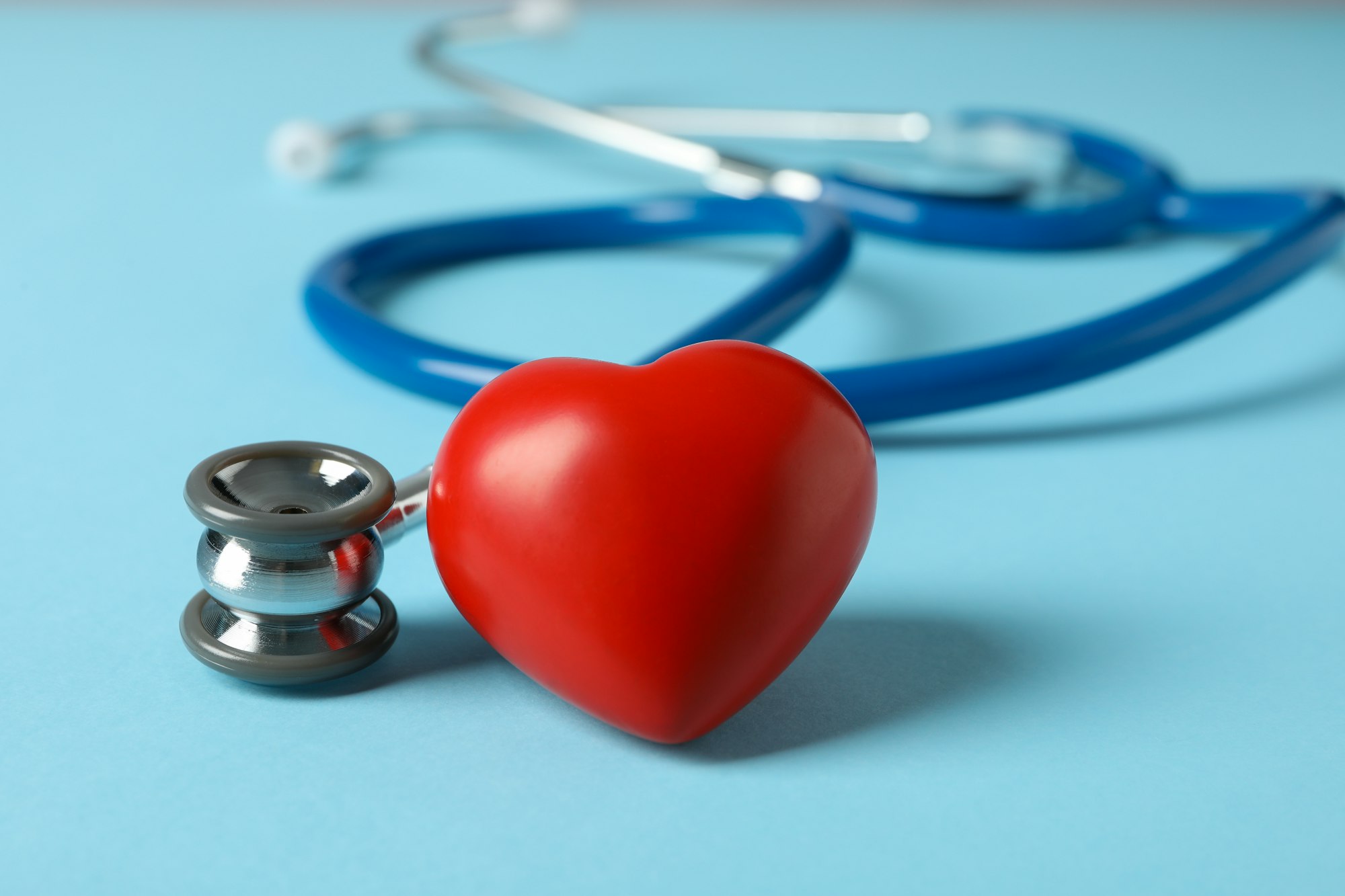 Stethoscope and heart on blue background, close up