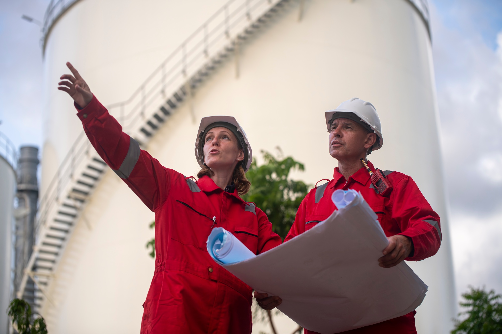 Engineers wearing safety gear, including hard hats examining survey a large blueprint tablet standin